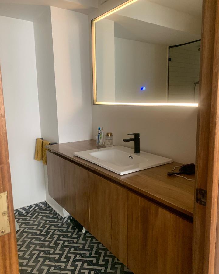 Baño con espejo LED, vanitorio de madera y piso espiga